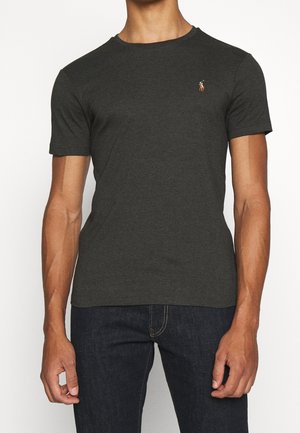 Mann trägt ein dunkelgraues kurzärmliges T-Shirt mit Rundhalsausschnitt und kleinem gestickten Polo-Spieler-Logo auf der linken Brust sowie dunkelblaue Jeans.