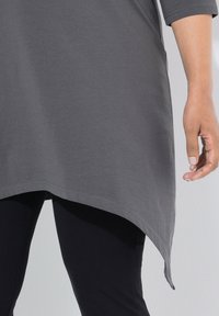 Harmaa tunika, joka on valmistettu pehmeästä puuvillasta, jossa on kaareva helma ja kolmanneksen mittaiset hihat. Käytetään tummien legginsien päällä.