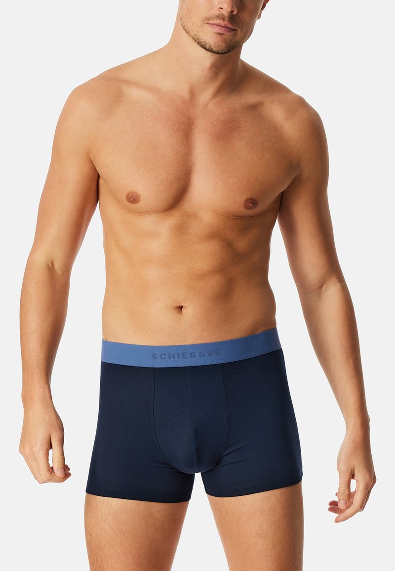 Marinblå boxershorts i mjuk tyg, med ett ljusblått elastiskt midjeband där "SCHIESSER" texten är i grått. Tätt sittande design.