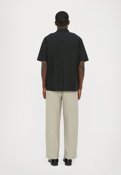 Black short-sleeve shirt with a straight cut, paired with light beige wide-leg trousers and black shoes, viewed from the back.