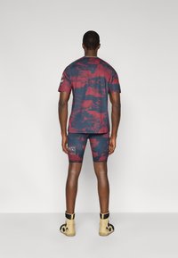 Αθλητική ενδυμασία ανδρών με κοντομάνικη μπλούζα σε κόκκινο και μπλε σχέδιο, ταιριαστά σορτς και μπεζ παπούτσια με μαύρες λεπτομέρειες.