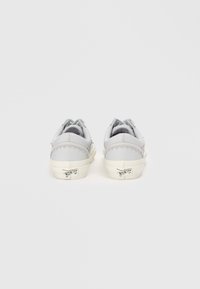 Sneakers din piele gri, cu o talpă din cauciuc alb, cusături decorative și un logo pe călcâi, având un design de tip low-top.