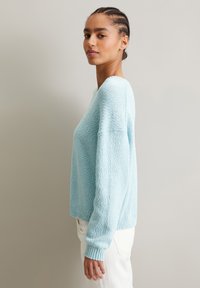 Hellblauer Strickpullover mit strukturiertem Finish, Rundhalsausschnitt und gerippten Manschetten. Lockere Passform, Dreiviertelärmel und gerade Saum.