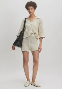 Lichtcrème gebreide oversized top met een kraag, gecombineerd met bijpassende gestructureerde shorts en platte instappers. Zwarte schoudertas inbegrepen.