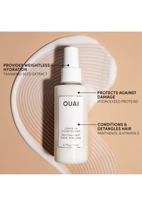 Flacon de leave-in conditioner Ouai sur une surface beige incurvée avec un texte mettant en avant l'hydratation, la protection contre les dommages et les bienfaits démêlants pour les cheveux.