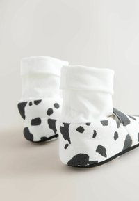 Zapatillas con estampado de vaca en blanco y negro, con parte superior de tela suave, puños blancos enrollados y suelas negras. Diseñadas para brindar comodidad y calidez.