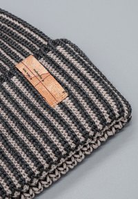 Cappellino lavorato a maglia a righe grigie e beige, con una finitura testurizzata e un'etichetta rettangolare in tessuto arancione con dettagli stampati.