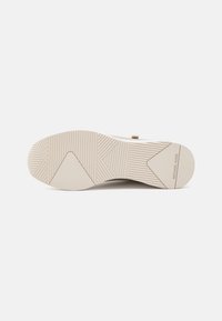 Suola di sneaker beige con scanalature testurizzate e un motivo geometrico. Presenta un dettaglio di branding discreto e una punta liscia e arrotondata.