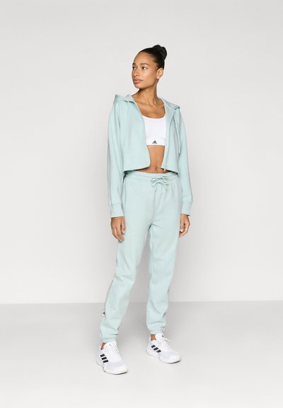 Ανοιχτό πράσινο cropped φούτερ με κορδόνια, σε συνδυασμό με ταιριαστά joggers. Διαθέτει λεία υφή και λευκές λεπτομέρειες στα παπούτσια.