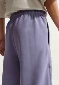 Pantalon de survêtement violet clair avec une taille élastique, des poches latérales et une texture lisse, offrant une coupe décontractée et des détails de couture nets.