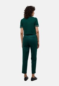 Polo en maille vert foncé avec des rayures blanches sur le col, associé à un pantalon cropped slim vert foncé et des chaussures plates noires.