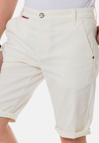 Shorts en coton blancs avec des ourlets roulés, des poches avant et une fermeture à bouton métallique. Présente des détails surpiqués légers et une texture douce.