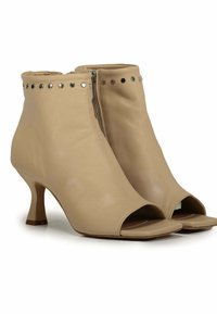 Stivaletti beige in pelle con retro chiuso, punta aperta e tacco basso. Presentano borchie argentate lungo la parte superiore e una cerniera laterale.