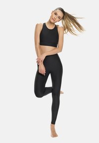 Set di abbigliamento attivo nero composto da un top corto e leggings a vita alta, entrambi realizzati in un tessuto morbido ed elasticizzato con una finitura opaca.