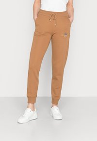 Bruna sweatpants med elastiskt midjeband, dragsko, två sidofickor och ribbade muddar. Har en liten logotyp framtill.