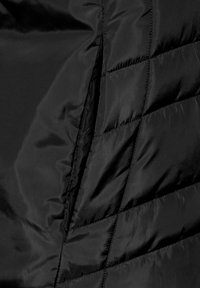 Chaqueta negra acolchada con una textura suave y brillante, que presenta patrones de costura diagonal y un detalle de cremallera oculta en el lateral.