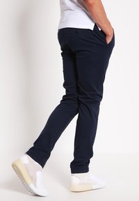 I chinos blu navy presentano una vestibilità slim, una trama liscia e tasche frontali. Dettagli notevoli includono un piccolo bottone sul retro e un design su misura.
