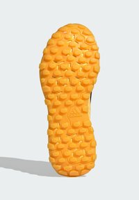 Żółta podeszwa sportowego buta z teksturowanym wzorem heksagonalnych i trójkątnych kolców zapewniających przyczepność. W centralnej części znajduje się wytłoczone logo.