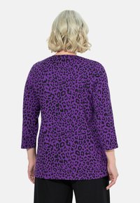 Lila Langarmshirt mit schwarzem Leopardenmuster, das einen lockeren Schnitt und einen runden Halsausschnitt aufweist. Strukturierter Stoff mit 3/4-Ärmeln.