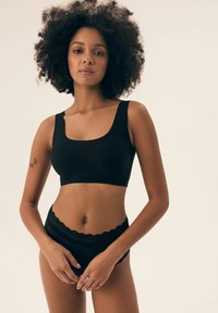 Schwarzer Bralette mit breiten Trägern und quadratischem Ausschnitt, kombiniert mit schwarzen Unterhosen mit Spitzendetails aus weichem Stoff und schmaler Passform.