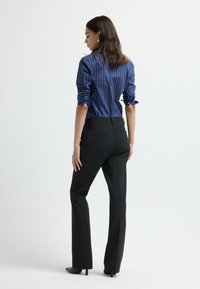 Marine gestreepte shirt met opgerolde mouwen, in combinatie met zwarte broeken. De outfit heeft een aansluitende snit en een soepel materiaal.