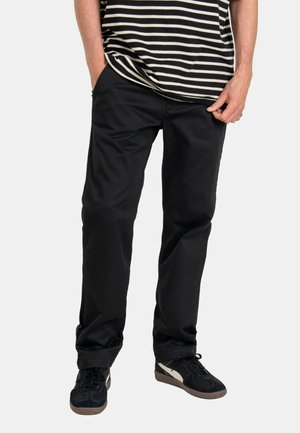 Schwarze Hose mit geradem Schnitt, aus robustem Stoff gefertigt. Verfügt über seitliche Taschen und gestickte Details. Kombiniert mit dunklen Sneakers und einem gestreiften Hemd.