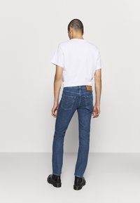 Blå jeans i denim med en figurnära passform, raka ben och en läderlapp på bakre midjebandet. Kombinerade med en enkel vit t-shirt och svarta stövlar.