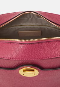 Interno di una borsa in pelle rosa con una cerniera dorata e un'etichetta in pelle che mostra il nome del marchio. Esterno testurizzato con una finitura liscia.