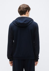 Sudadera con capucha azul marino hecha de tela suave, con una capucha grande, puños acanalados y un ajuste relajado, diseñada para comodidad y libertad de movimiento.