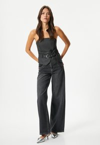 Top gris sin mangas con cinturón en la cintura, combinado con jeans oscuros de corte holgado. La modelo lleva tacones plateados, resaltando una estética moderna.