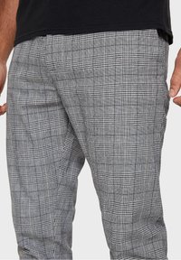 Pantaloni a quadri grigi realizzati in tessuto testurizzato, con una combinazione di quadretti piccoli e grandi in bianco e nero, dotati di tasche laterali.