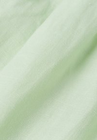 Tissu vert clair avec une texture douce et tissée, montrant des plis et des ombres subtiles sur la surface.