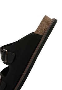 Sandalo nero in materiale scamosciato, con soletta in sughero e fibbia metallica regolabile. Caratterizzato da lati aperti e suola in gomma testurizzata.