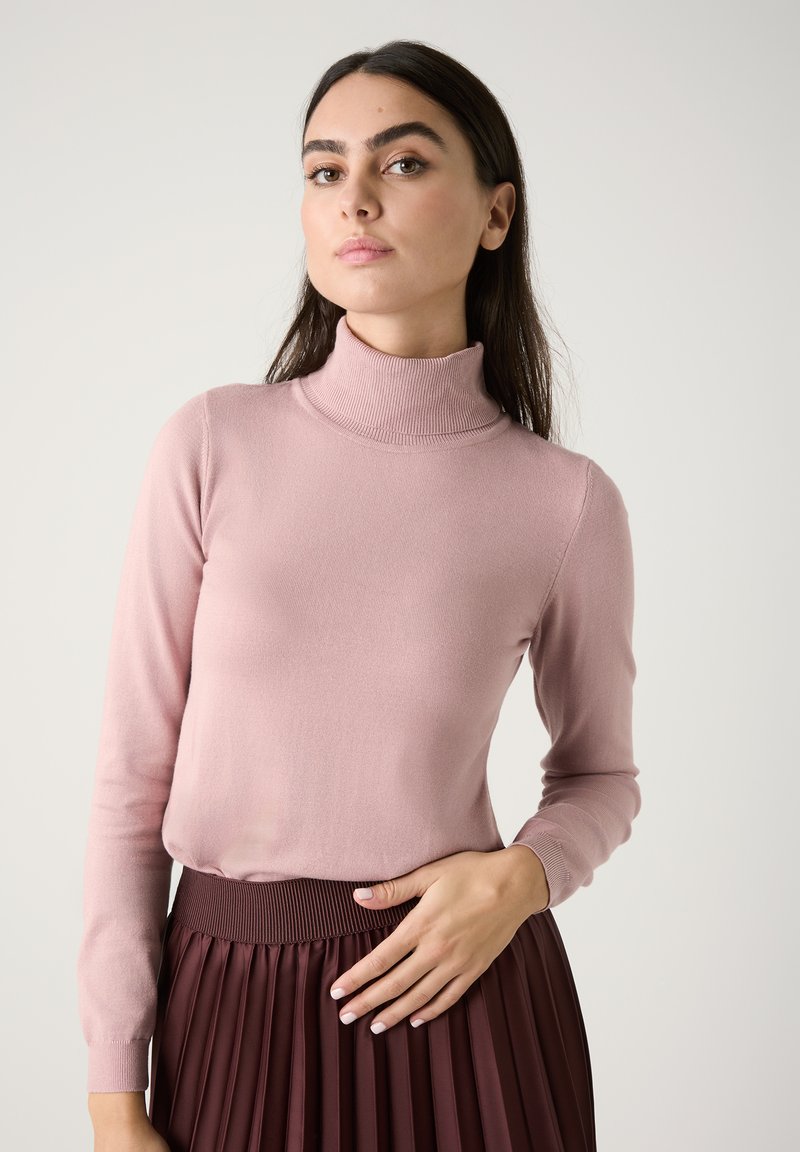 Helle rosa Rollkragensweater aus weichem Stoff, figurbetonte Silhouette, lange Ärmel, kombiniert mit einem dunklen, plissierten Rock und geripptem Taillenbund.