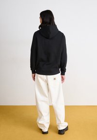 Zwarte hooded sweatshirt met een ontspannen pasvorm, gecombineerd met crègekleurige oversized broek met een achterzak en logo-applicatie.