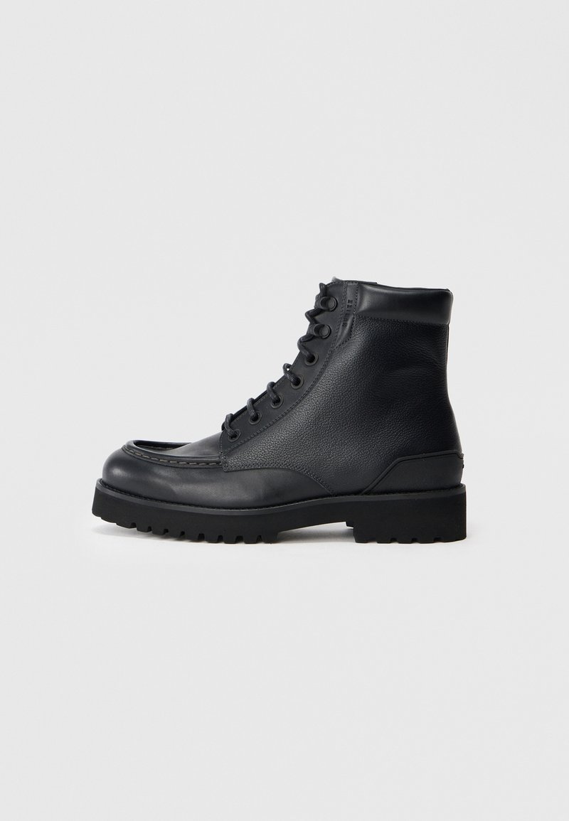 Botas de tobillo de cuero negro con un acabado liso y texturizado, punta redonda, diseño con cordones y suela resistente para mejorar el agarre y la durabilidad.