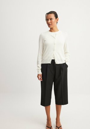 White button-up cardigan made of soft fabric, styled with black wide-leg cropped trousers, showcasing a relaxed, contemporary silhouette.