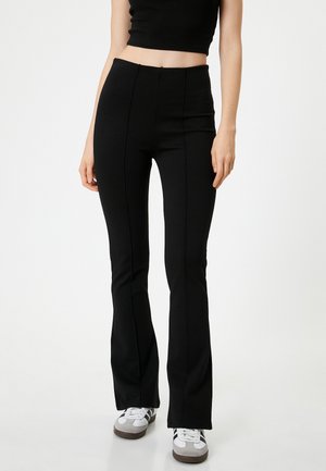 Pantalones acampanados negros hechos de una tela elástica. Presentan un diseño de cintura alta con costuras visibles y una textura suave. Combinados con zapatillas blancas.
