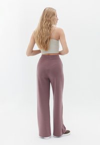 Blassgrünes, kurzes Oberteil und lockere, lavendelfarbene Hose mit elastischem Bund. Glattes Material, minimalistisches Design und gerade Beinform.