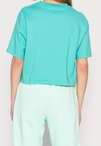 Camiseta corta de color turquesa claro con mangas cortas, material de algodón suave, cuello redondo y dobladillo limpio. Combinada con pantalones de color menta claro.