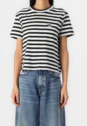 Persoon draagt een zwart-wit gestreept shirt met korte mouwen met een klein patchlogo en wijde, hooggesneden blauwe spijkerbroek.