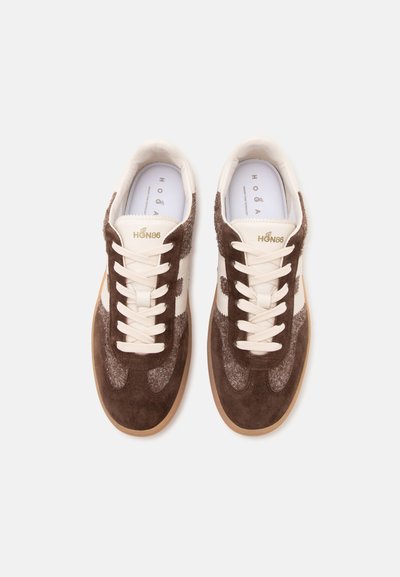 Paire de baskets en suède marron et beige avec des lacets blancs et des semelles en gomme, vues de dessus sur un fond blanc uni.