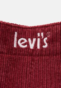 Tessuto a coste color bordeaux con il logo del marchio "Levi's" ricamato in bianco e il simbolo del marchio registrato vicino al bordo superiore.