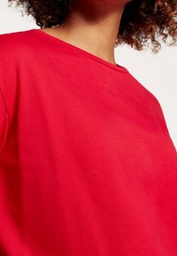 Punainen lyhythihainen paita, joka on valmistettu sileästä kankaasta. Siinä on pyöreä pääntie ja rento malli, ja se on yksivärinen ilman näkyviä kuvioita tai yksityiskohtia.