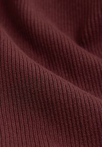 Burgunderfarbener, gerippter Stoff mit einer strukturierten Oberfläche, der feine, vertikale Linien und weiche, gewebte Fäden zeigt.