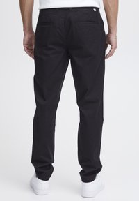 Pantaloni negri din bumbac cu un design drept, având două buzunare la spate și o textură netedă. Purtați cu adidași albi.