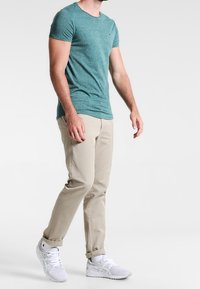 Teal short-sleeve t-shirt, beige chinos with rolled cuffs, and white sneakers. Cotton material, fitted design, minimal detailing.