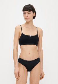 Černá braletka s krajkovým lemem a jemnou žebrovanou texturou s nastavitelnými ramínky, v kombinaci s černými bikinovými kalhotkami se zvlněnými okraji.