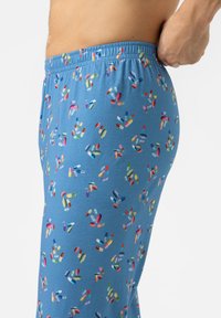 Lichtblauwe pyjamabroek met een pillenpatroon in verschillende kleuren. De stof is zacht en heeft een elastische tailleband. Zijkantzakdetails zijn zichtbaar.