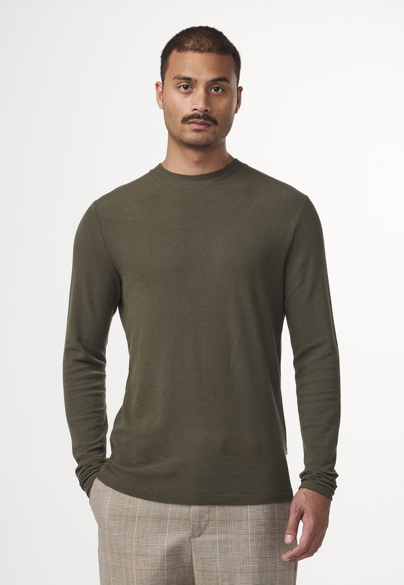 Camicia a maniche lunghe di colore verde oliva, con tessuto texturizzato, scollatura rotonda e maniche aderenti, abbinata a pantaloni con fantasia.